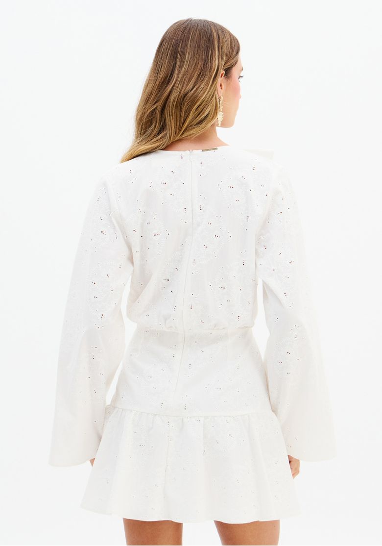 Modelo em pé usando vestido curto branco bordado de manga longa com decote V e sandália gladiadora de tiras