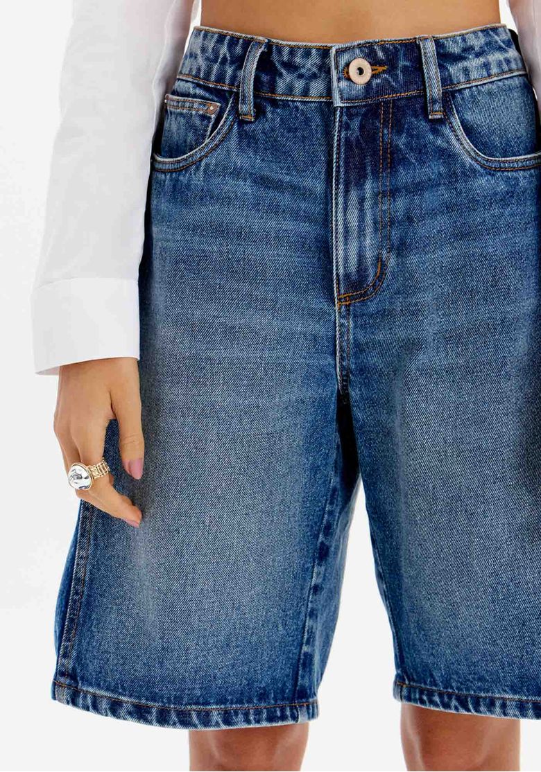 Close frontal da bermuda jeans feminina azul de cintura alta com botão, passantes e bolsos frontais funcionais