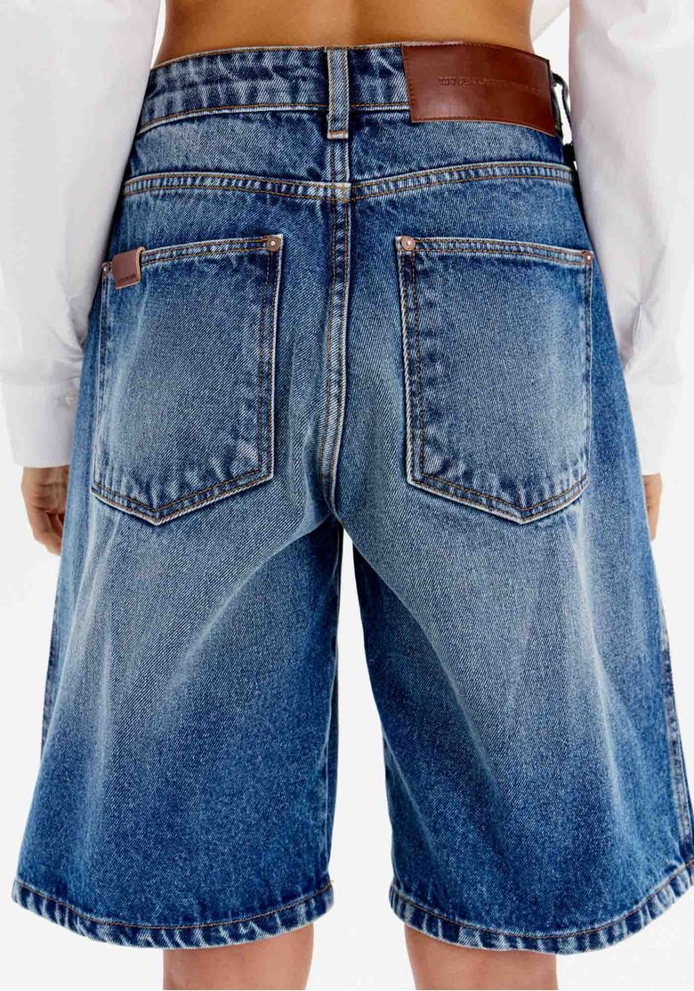 Close traseiro da bermuda jeans azul alongada com bolsos traseiros chapados e lavagem estonada