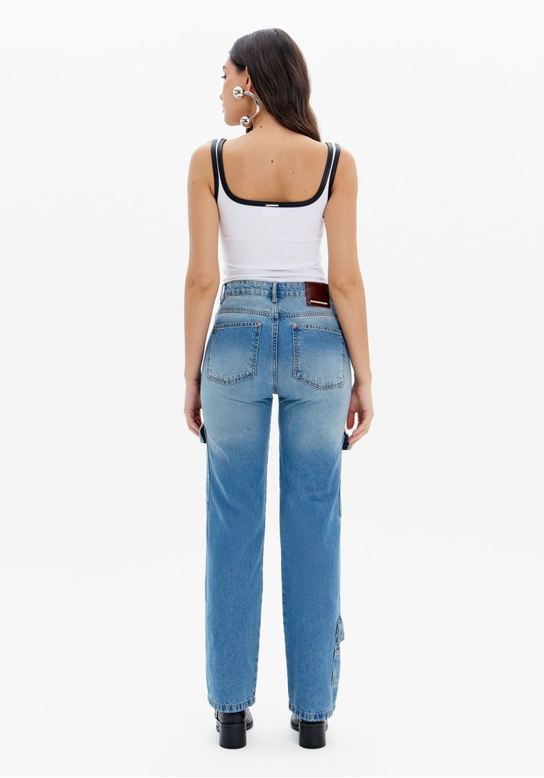 Detalhe frontal da calça jeans com bolso cargo lateral e recortes utilitários, tecido denim lavagem média e acabamento em bolso com aba