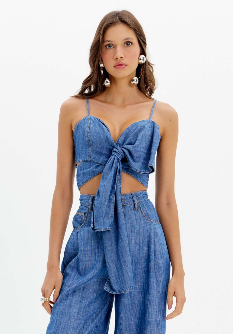 Modelo vestindo um top jeans cropped com laço frontal e decote coração em denim azul médio, vista frontal com calça jeans cintura alta.