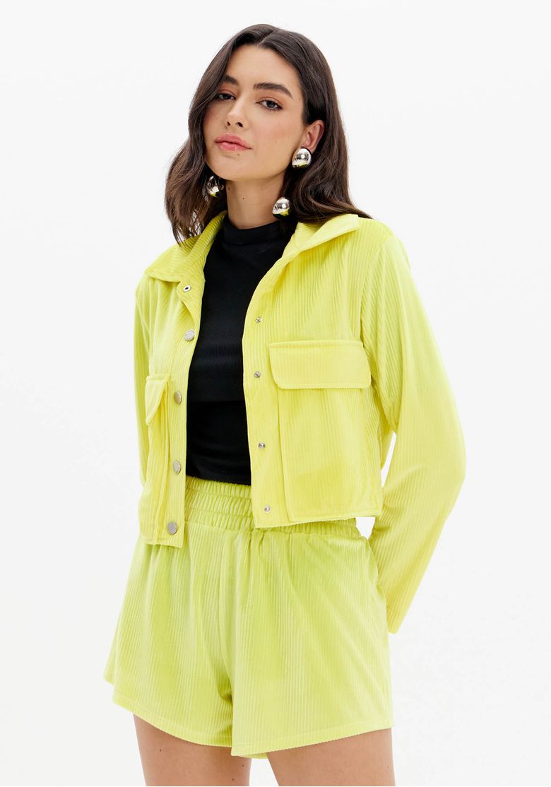 Modelo veste jaqueta cropped veludo amarelo claro vista 3/4 frontal com bolsos utilitários e top preto por baixo, look urbano