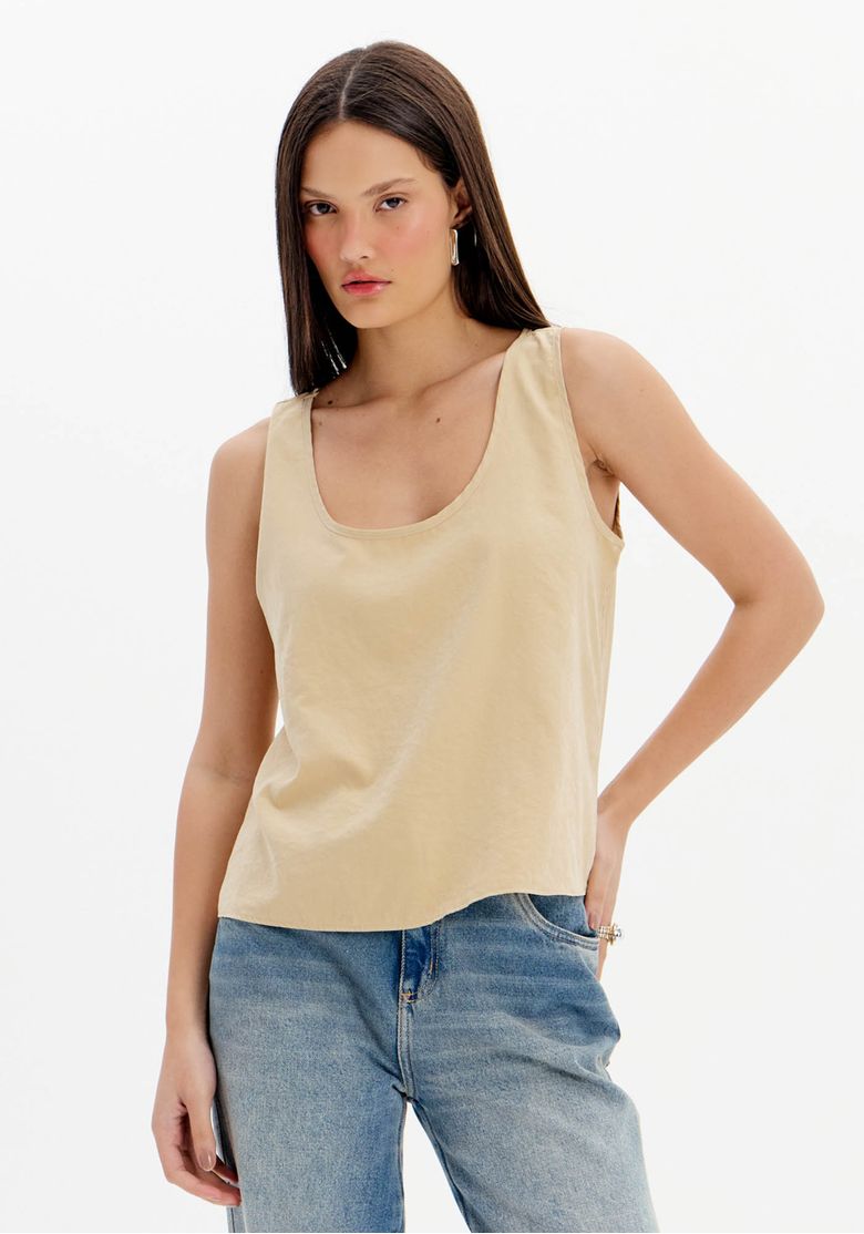 Modelo usando blusa sem mangas bege feminina de comprimento curto com decote U e caimento regular, combinada com calça jeans clara