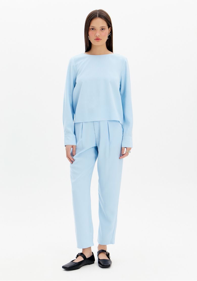 Modelo vestindo uma calça baggy azul com cintura alta e pregas frontais, combinada com uma blusa de tecido leve.