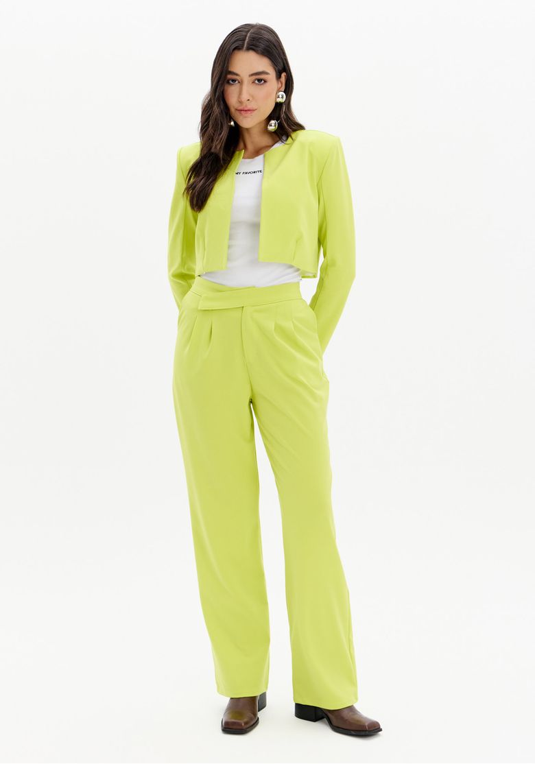 Modelo veste calça reta com cós assimétrico preta e blazer cropped, visão frontal em estúdio com tecido plano pesado