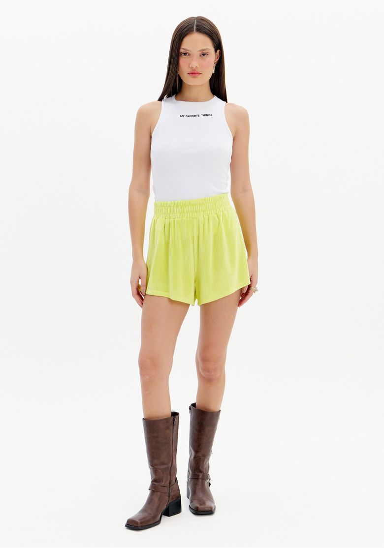Modelo em pé vestindo short boxer em veludo verde claro frontal, cintura alta com cós elástico largo, regata branca e botas marrom - look casual e sporty.