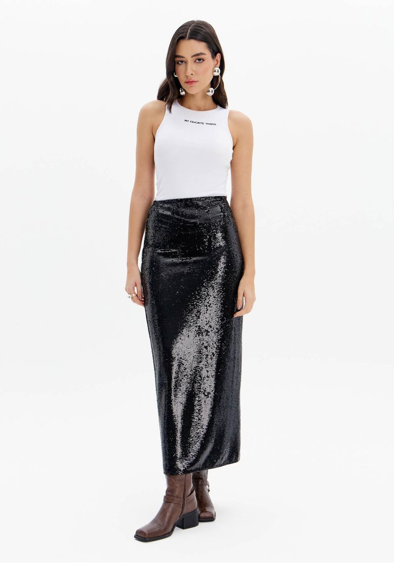 Modelo de frente usando saia super midi paetê preta, top branco e botas marrons, look noturno