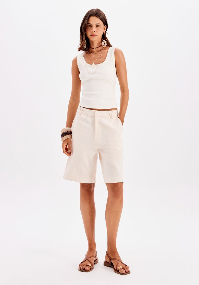 Modelo usando bermuda branca com top branco e sandálias.