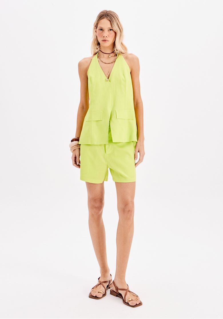 Imagem frontal full body da modelo usando conjunto com blusa frente única verde e shorts, look contemporâneo para work