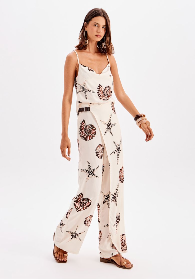 Modelo usando calça reta estampada feminina branca com estampa de conchas e estrelas-do-mar, cintura alta e sobreposição frontal, em look leve de verão