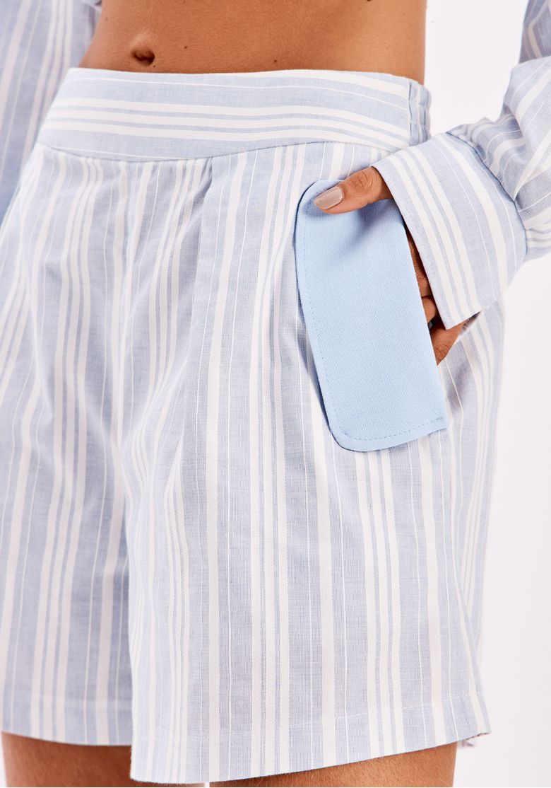Meio corpo da modelo com foco no short listrado azul e bolso lateral com aba contrastante em azul claro