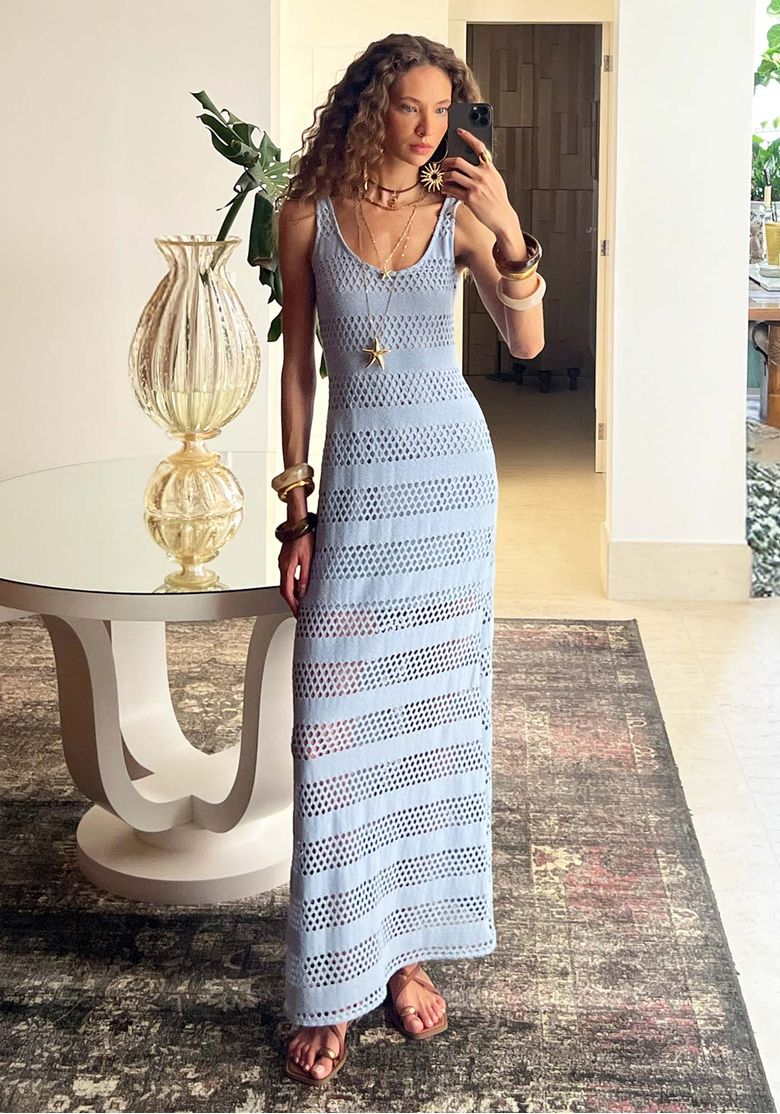 Foto lifestyle com modelo em ambiente interno usando vestido super midi de alças azul, look praiano sofisticado com acessórios