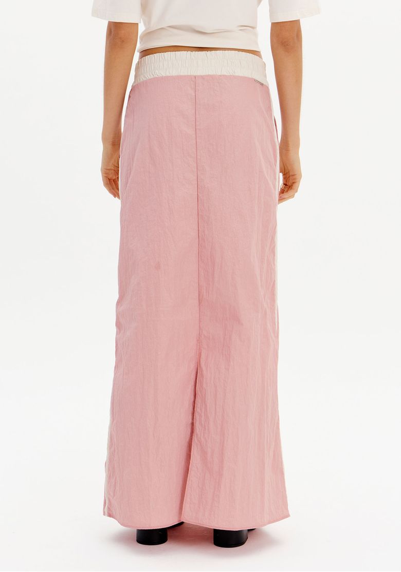 Modelo vestindo saia midi rosa com recortes e camisa branca vista de costas.
