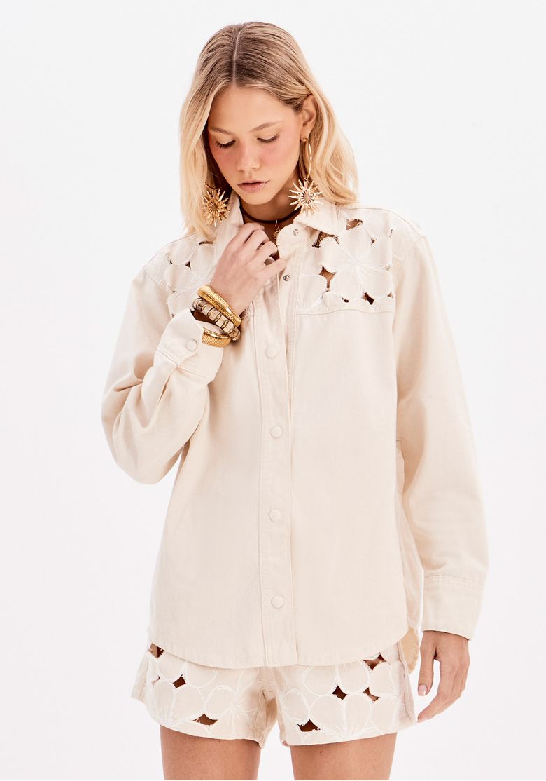 Modelo usando camisa feminina alongada branca em sarja com mangas longas, gola tradicional e recortes vazados florais, em foto frontal de e-commerce.