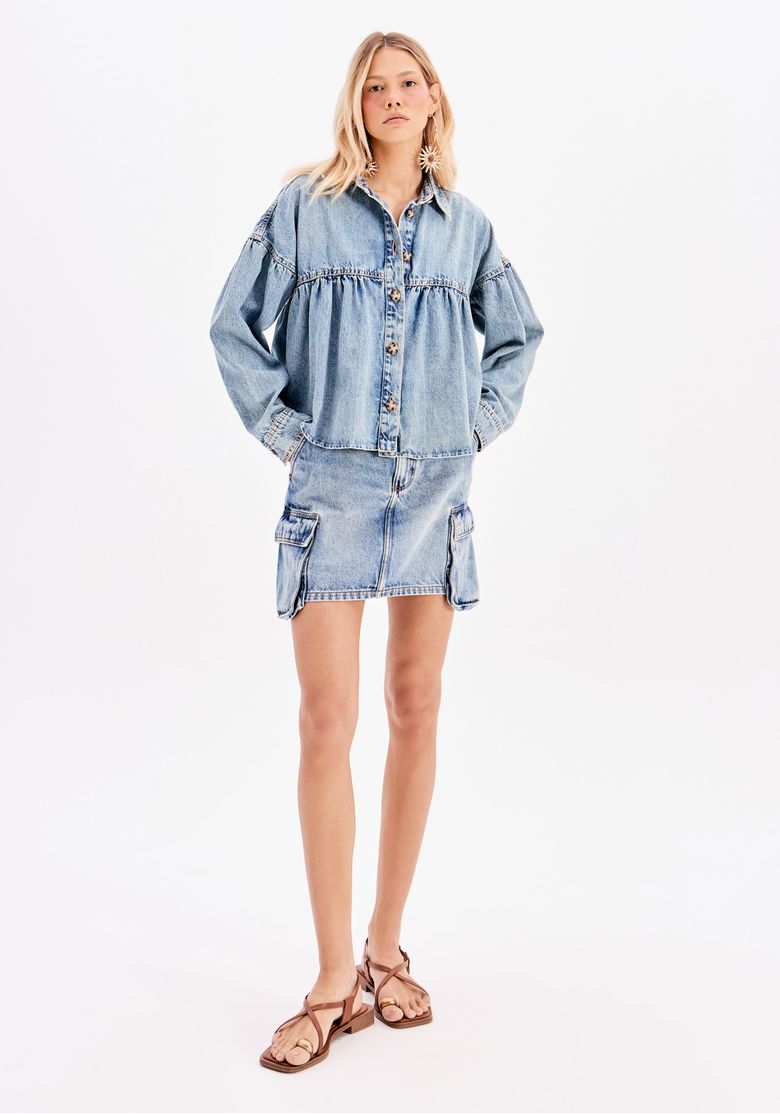 Modelo vestindo uma saia jeans cargo curta com cintura alta, confeccionada em denim estonado, combinada com jaqueta oversized e sandálias - um visual casual feminino.