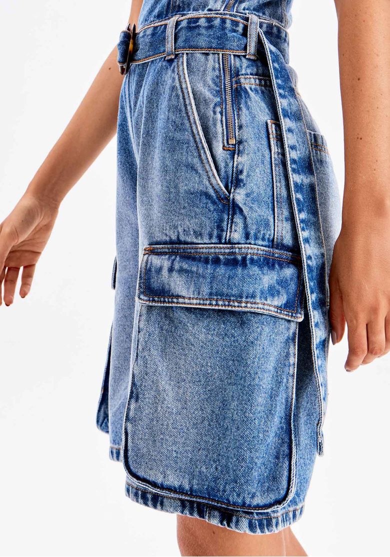 Close do bolso utilitário lateral do macacão curto jeans azul feminino com lavagem estonada e recortes