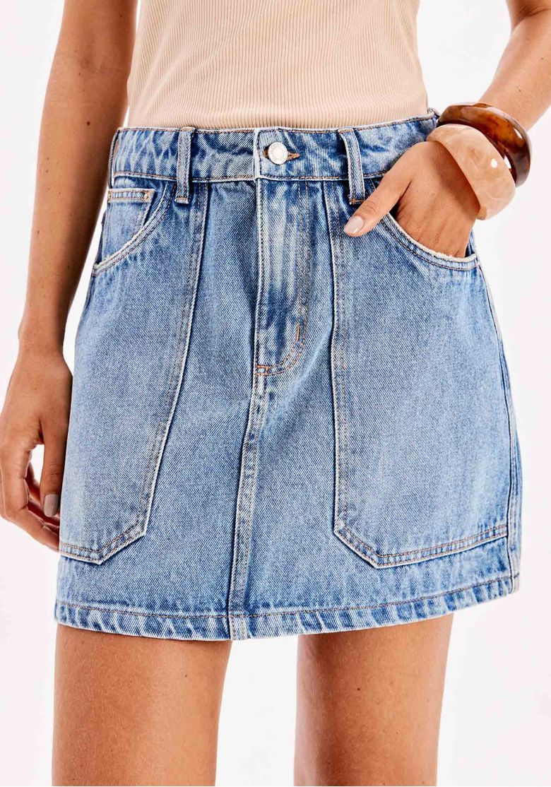 Detalhe da saia jeans curta mostrando os bolsos frontais e o cós com passantes.