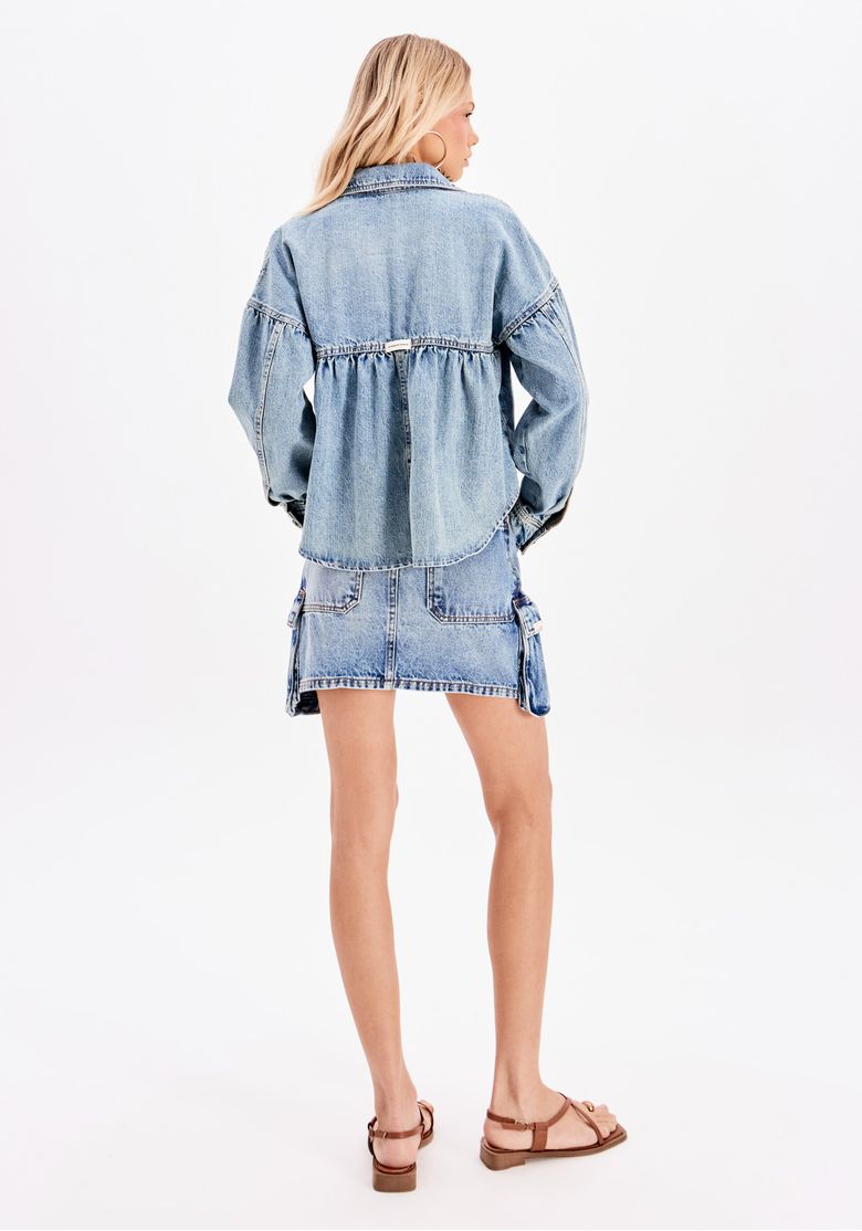 Detalhe do cós e dos bolsos laterais cargo da saia curta em denim, destacando o design com lapela e a costura da lavagem estonada.
