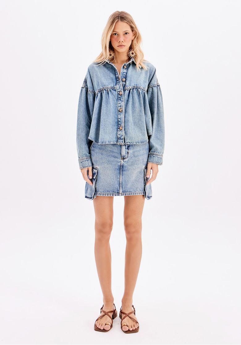 Vista traseira da modelo com a saia jeans cargo curta e uma jaqueta, mostrando o comprimento curto e os bolsos laterais cargo.
