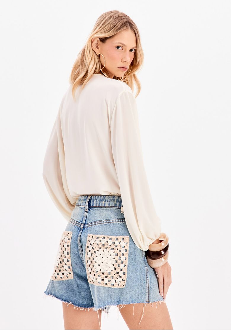 Modelo vista de costas usando short jeans azul cintura alta com bolsos traseiros em crochê manual e barra desfiada - short jeans cintura alta crochê
