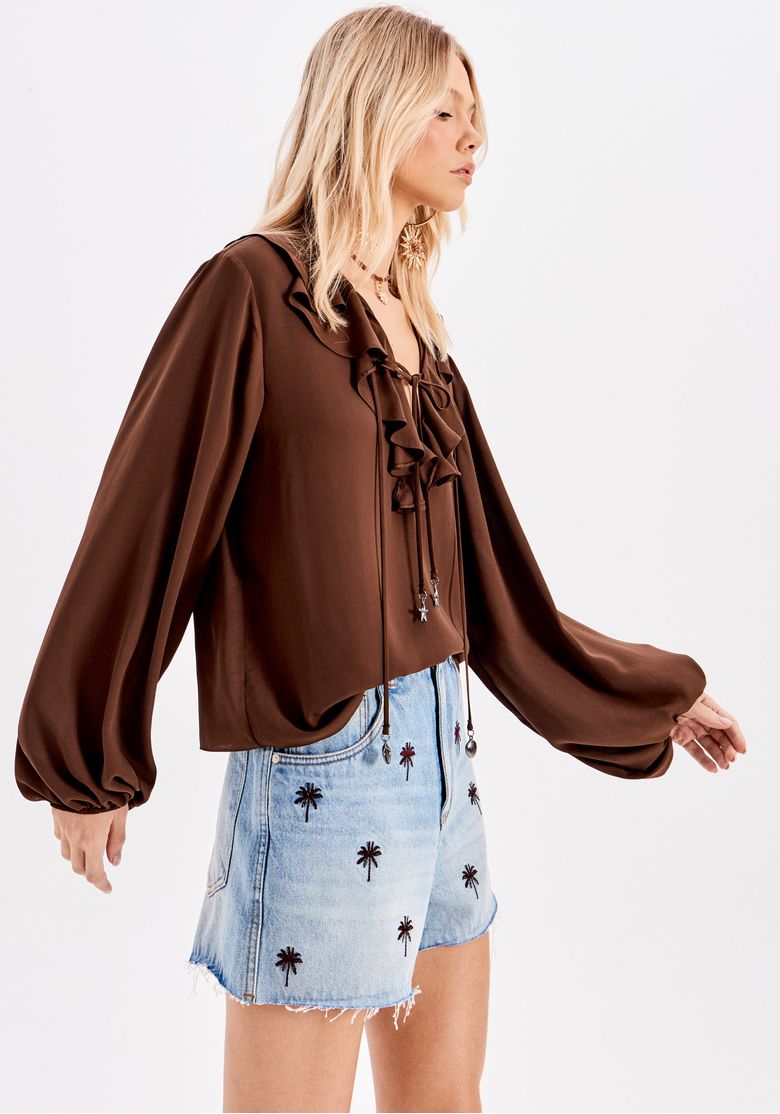 Vista lateral do short jeans com bordados e blusa marrom.