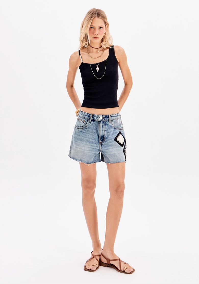 Modelo em pose casual vestindo short jeans mom e top preto.