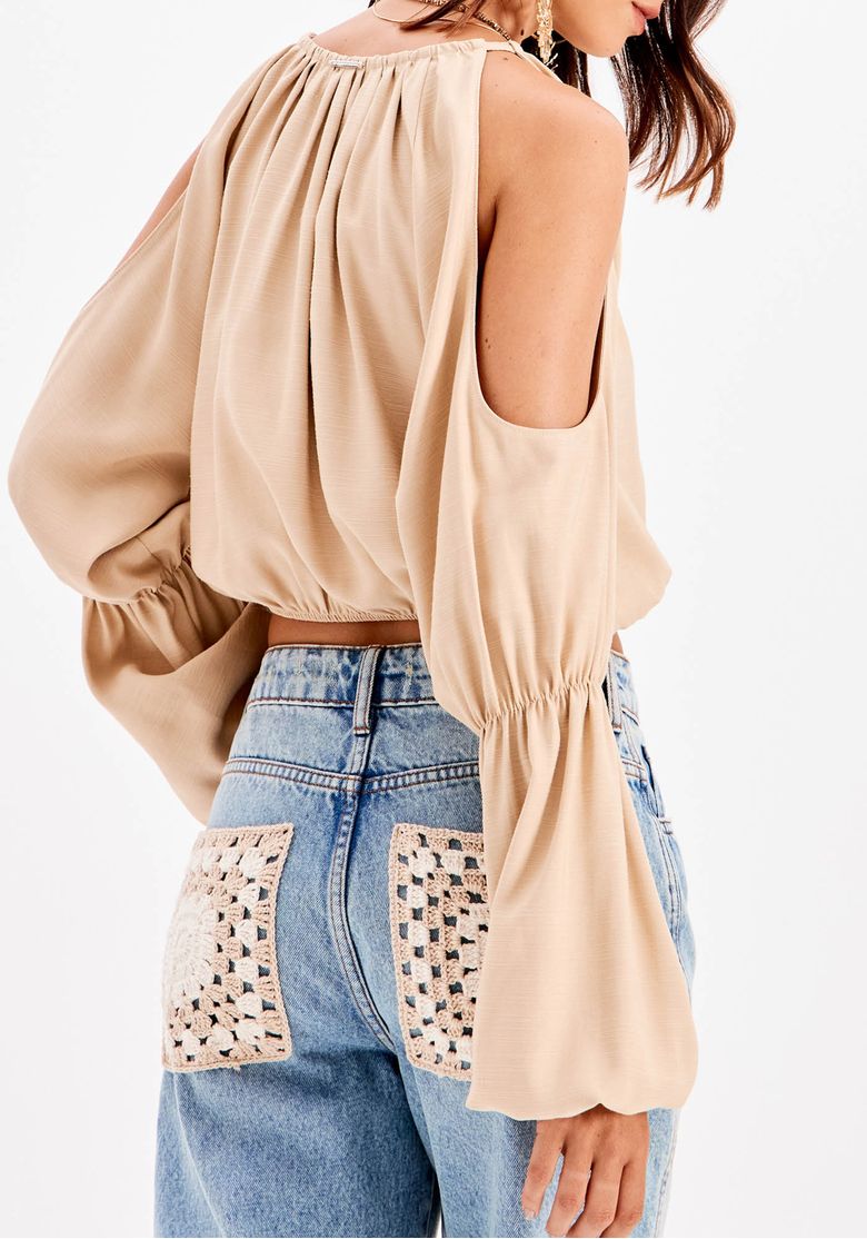 Detalhe lateral da blusa cropped bege com ombro vazado e manga ampla com punho elástico - acabamento fluido