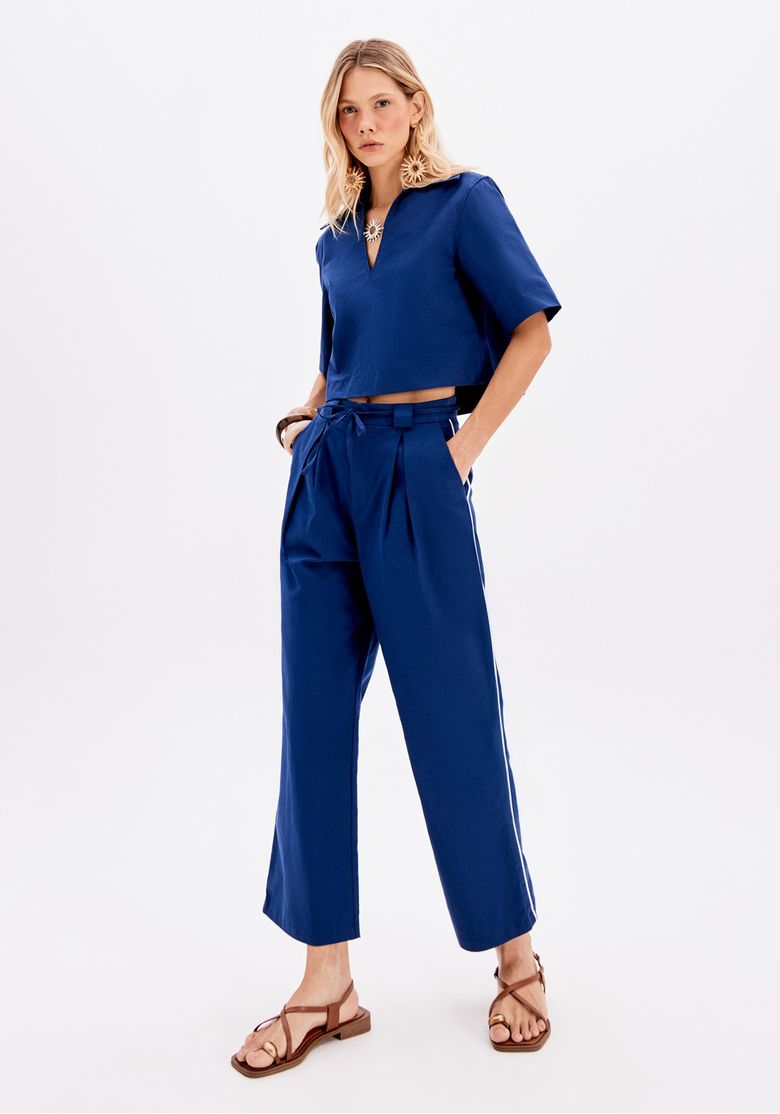 Look feminino com blusa cropped azul gola polo e calça azul de cintura alta com amarração, vista frontal completa