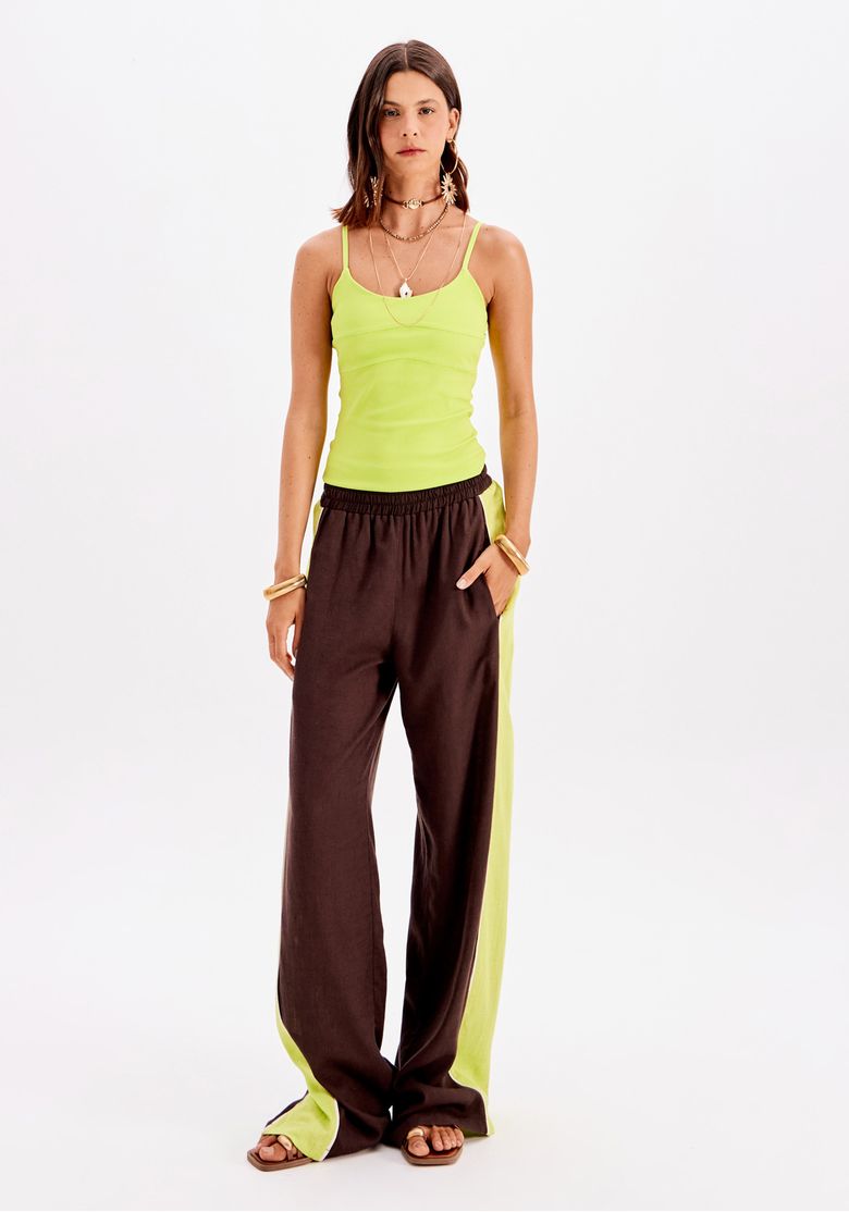 Modelo vestindo blusa ajustada verde com alças finas e calça esportiva marrom com detalhes laterais.