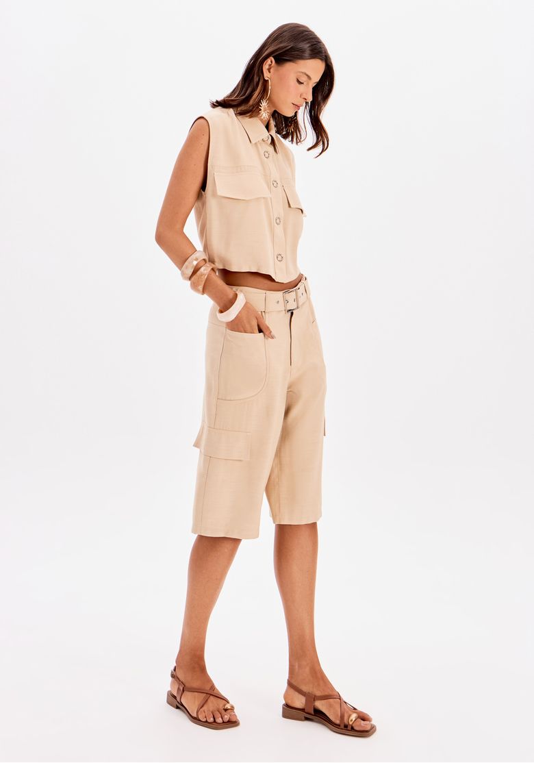 Look completo com camisa cropped sem mangas bege combinada com bermuda cargo de cintura alta e sandália rasteira marrom
