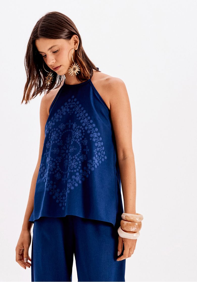 Modelo usando blusa frente única azul em tecido plano leve e calça pantalona, vista três-quartos frontal com estampa centralizada e caimento alongado