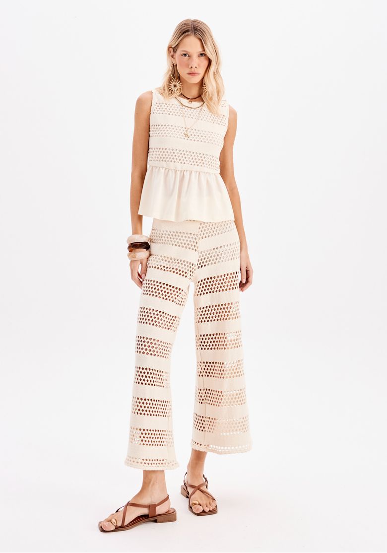 Modelo vestindo calça reta cropped off-white com padronagem vazada geométrica vista frontal, acompanhada de top regata off-white e sandálias rasteiras