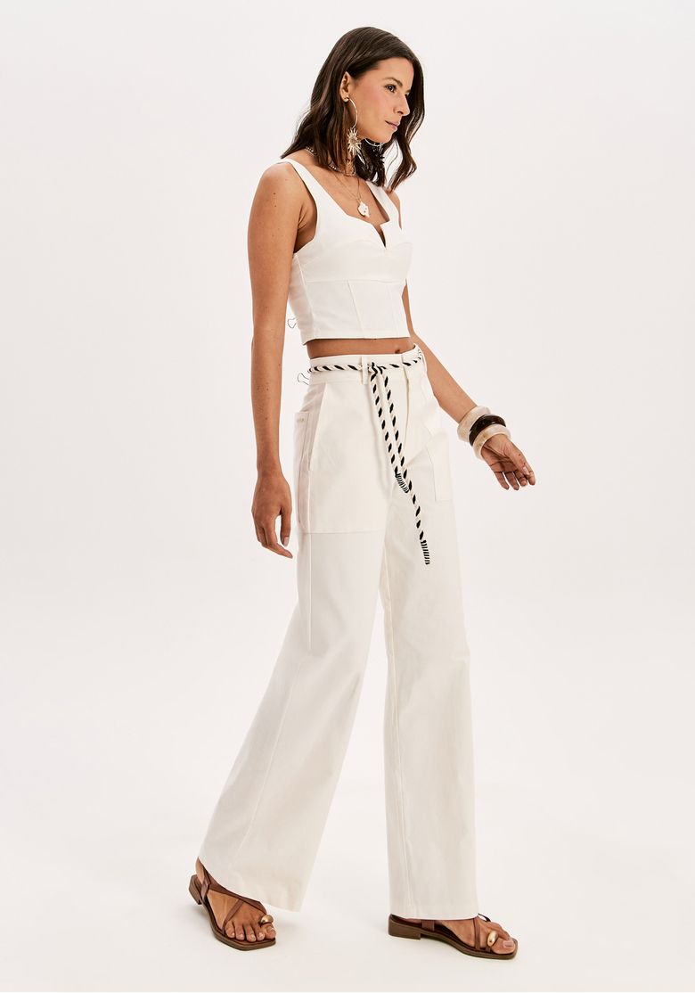 Vista lateral do look com calça reta branca de alfaiataria leve, bolsos amplos e sandália rasteira