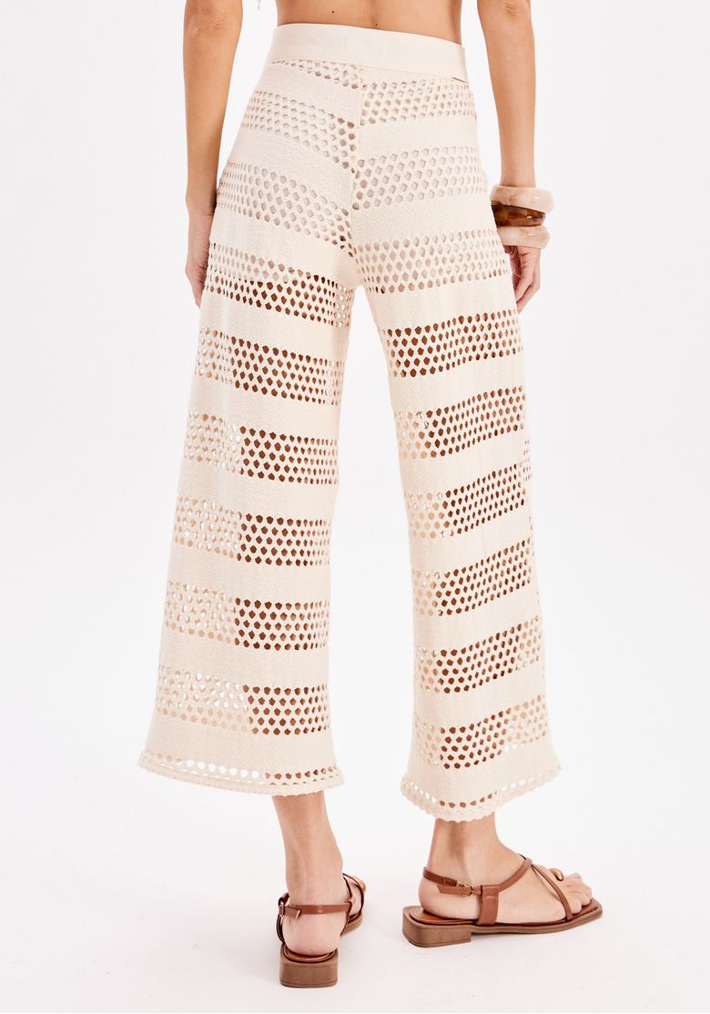 Close frontal do cós e das pernas da calça pantacourt vazada em linho off-white, evidenciando o padrão geométrico e o caimento