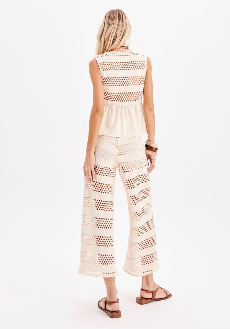 Modelo de costas usando top regata e calça reta vazada off-white em look verão, destacando o conjunto com textura aberta