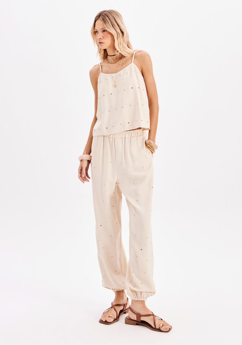 Modelo usando calça jogger feminina bege com aplicações e barra elástica, em look casual urbano com top de alças e sandálias