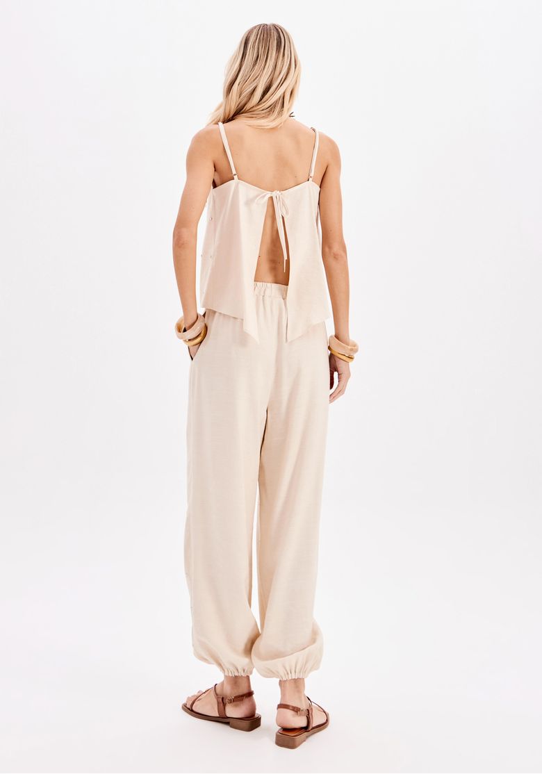 Vista traseira de look feminino com calça jogger bege de tecido leve e barra elástica, combinada com top bege de costas abertas