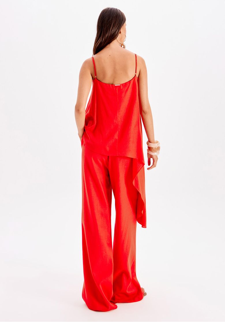 Perfil lateral do look com calça reta de linho vermelho e top assimétrico, evidenciando movimento do tecido