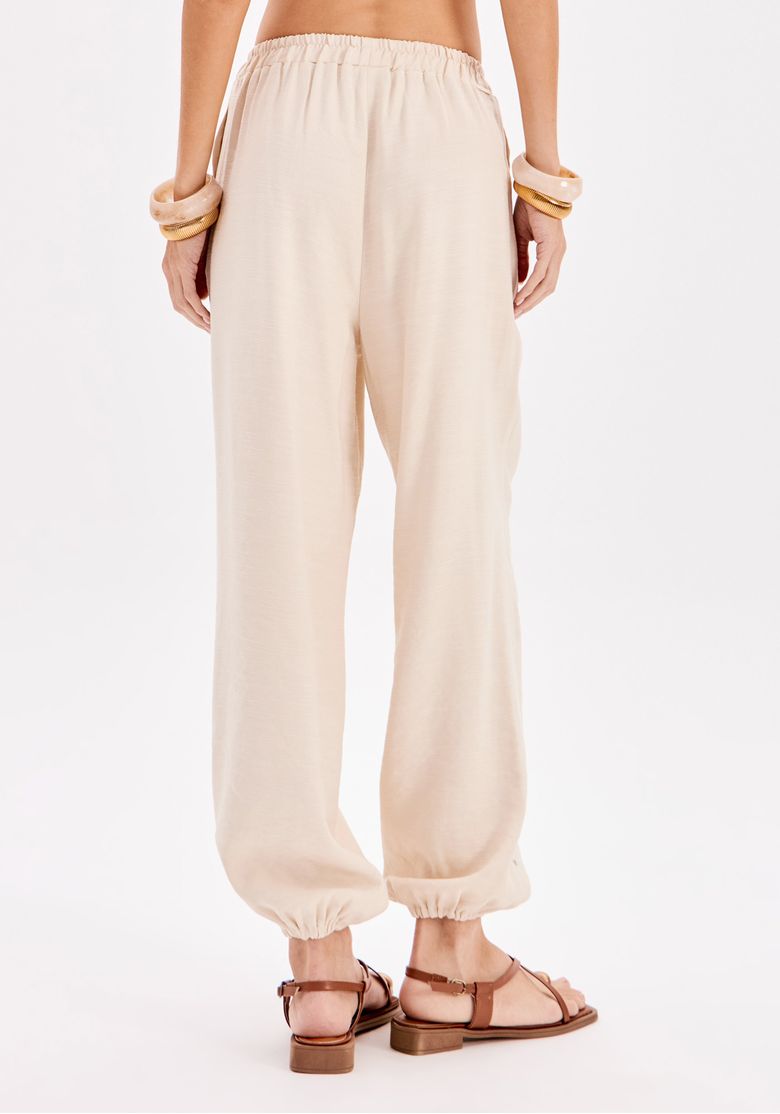 Close traseiro de calça jogger feminina bege com cós elástico e barra franzida, modelagem relaxed em tecido plano leve