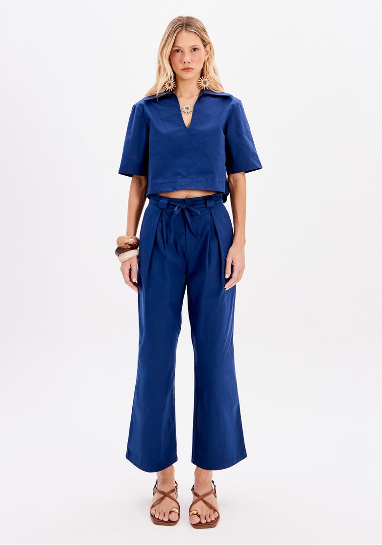 Modelo completa o look com blusa azul e sandálias, destacando a calça.