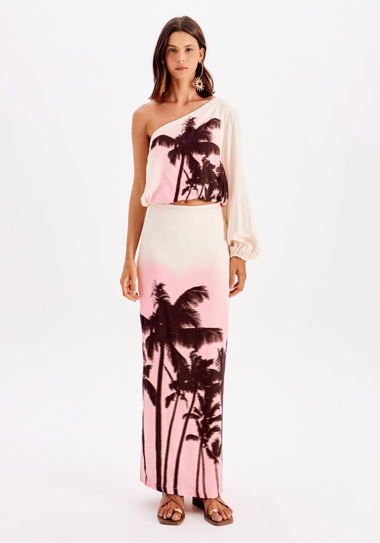 Modelo em look frente com saia super midi estampada de palmeiras em degradê rosa sobre branco e top ombro só, visual tropical e fresh