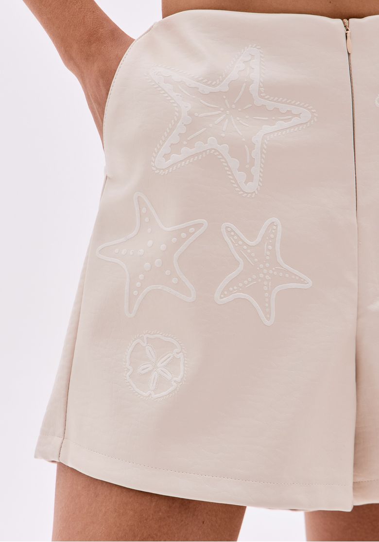 Detalhe das aplicações bordadas de estrelas-do-mar no short bege.