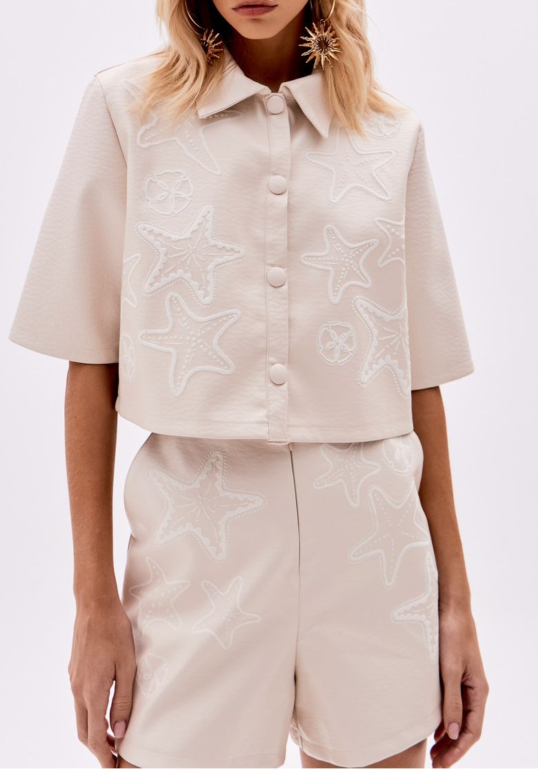 Camisa bege com aplicações bordadas de estrelas-do-mar, vista frontal.