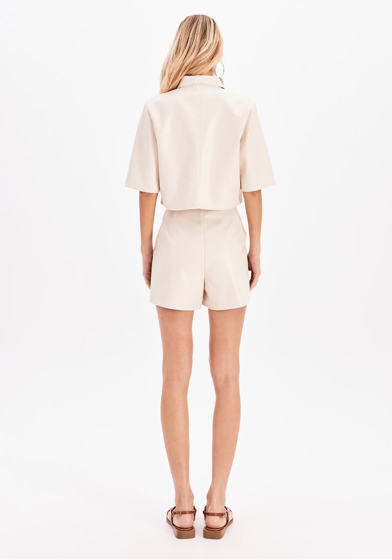 Vista traseira do conjunto com short e camisa bege com aplicações bordadas.