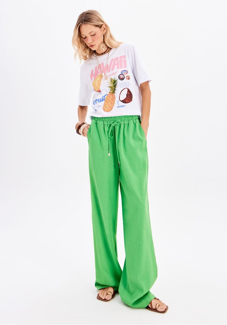 Modelo vestindo camiseta oversized branca com estampa colorida e calça verde vibrante.