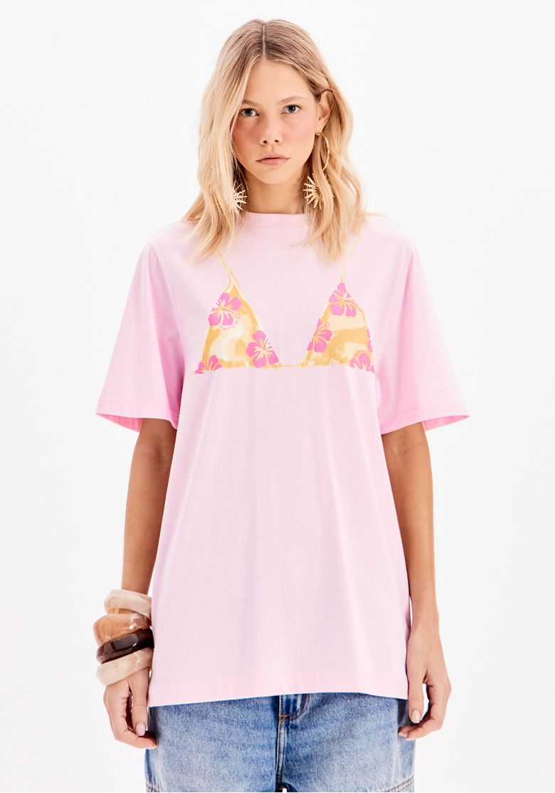Camiseta oversized rosa com estampa de biquíni vista de frente, destacando a modelagem ampla e mangas curtas.