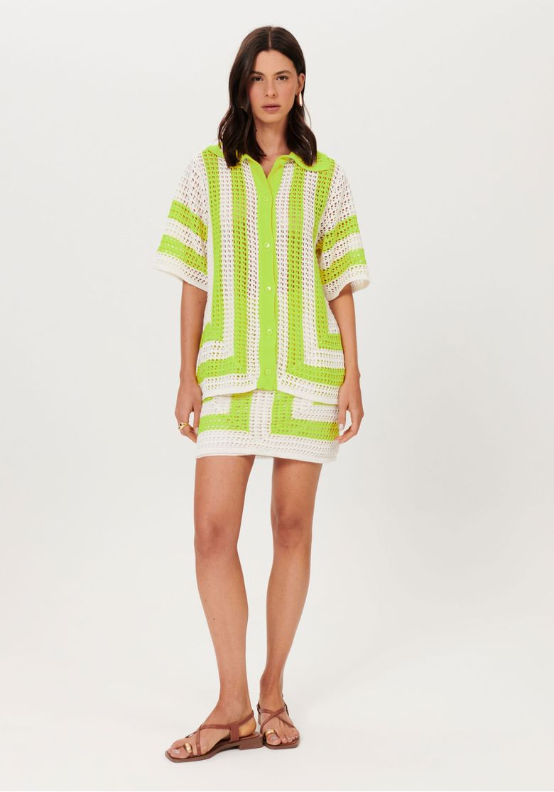 Modelo em look completo usando saia tricô curta bege com camisa de tricô combinando; visual verão com ponto vazado e listras geométricas