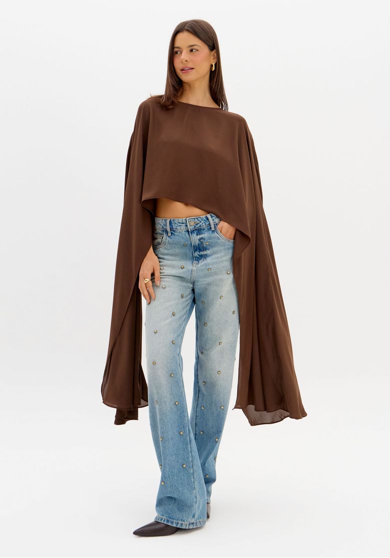 Modelo usando blusa cropped capa marrom feminina com caimento fluido e efeito dramático, combinada com calça jeans ampla