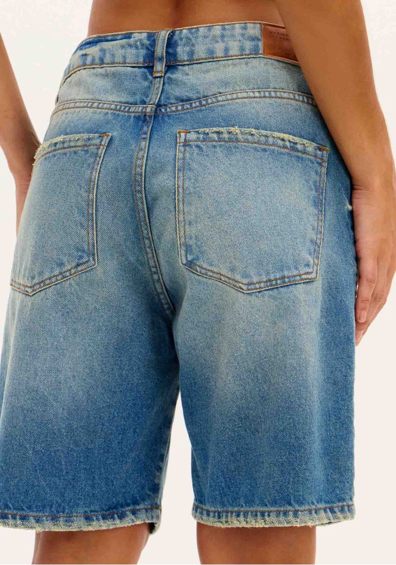 Vista lateral da bermuda jeans mostrando o comprimento e o ajuste.