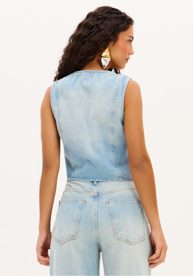 Modelo usando colete jeans feminino azul claro ajustado com botões aparentes, bolsos frontais e barra assimétrica